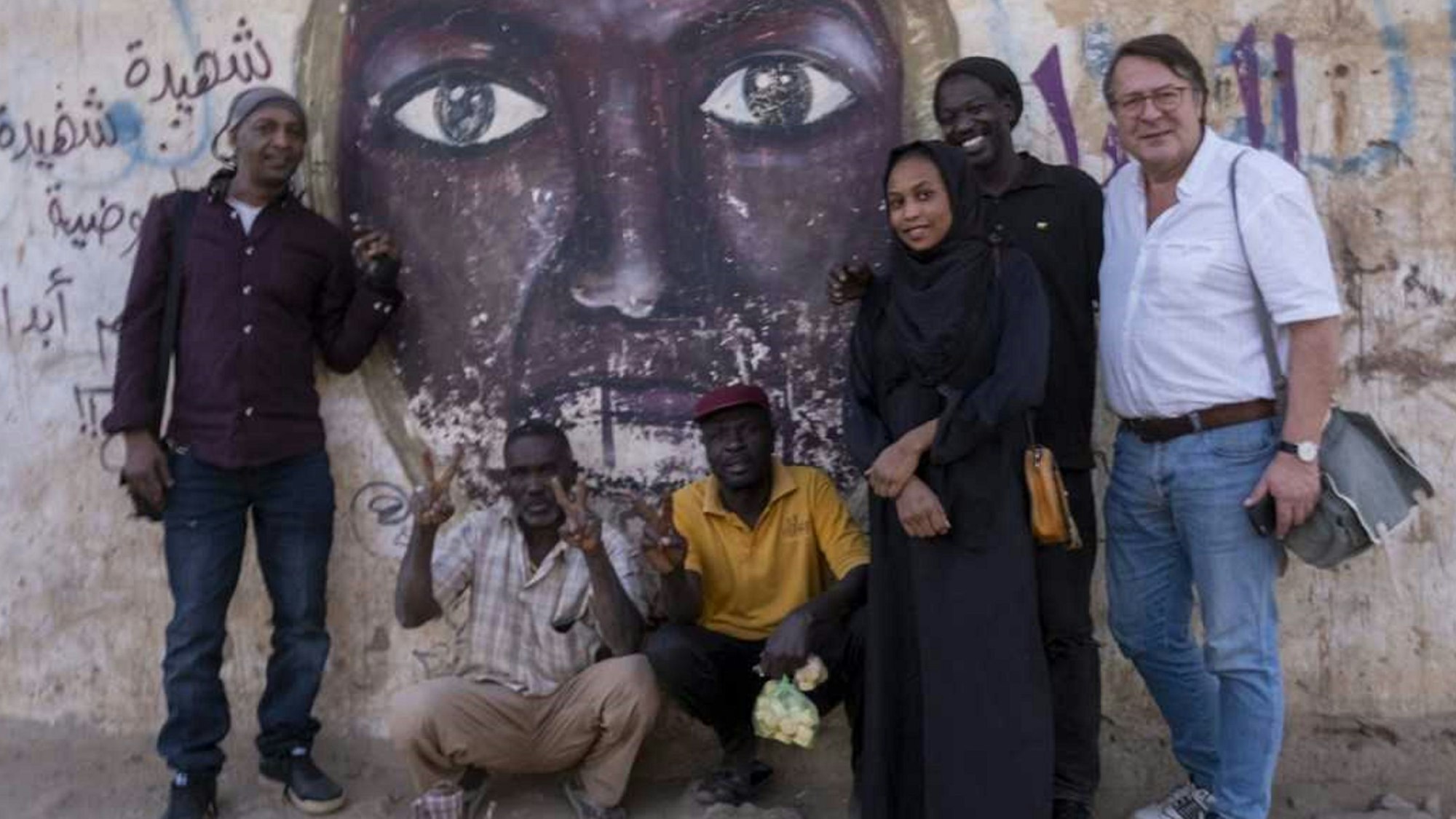 Hans Mörtter (r.) und Hassan Magdi (l.) mit anderen in Khartum vor einem Wandbild, das die 2012 erschossene Parlamentarierin Awasia Ajbna zeigt.