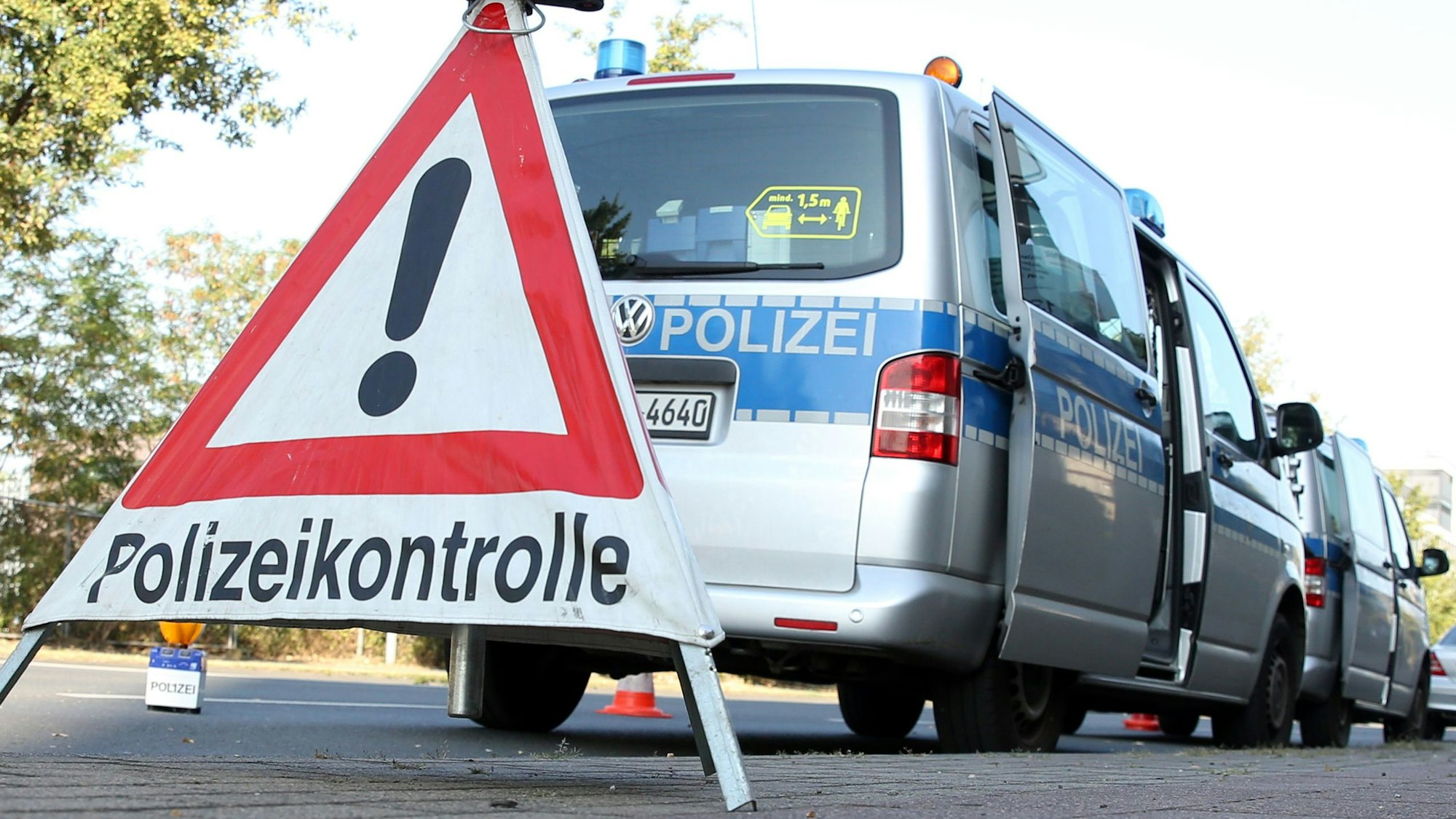 Polizeifahrzeuge parken an einer Straße. Im Vordergrund steht ein Schild mit der Aufschrift Polizeikontrolle.