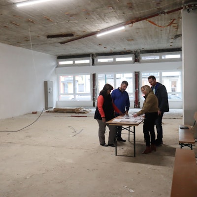 Vier Personen stehen an einem Tisch, der in einem Rohbau steht.