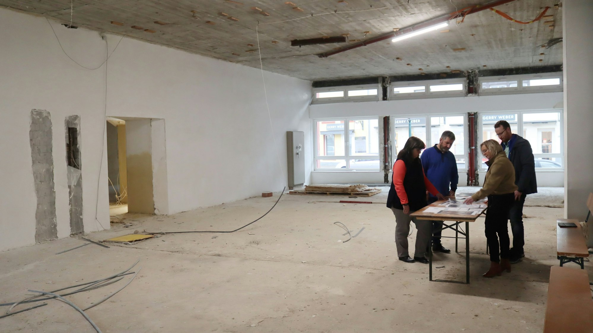 Vier Personen stehen an einem Tisch, der in einem Rohbau steht.