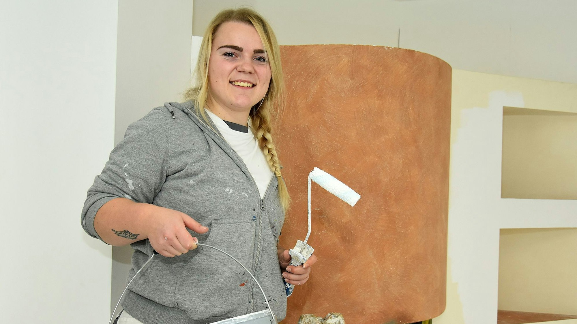 Malerin Nora Haase hält eine Farbrolle und einen Farbeimer in den Händen.