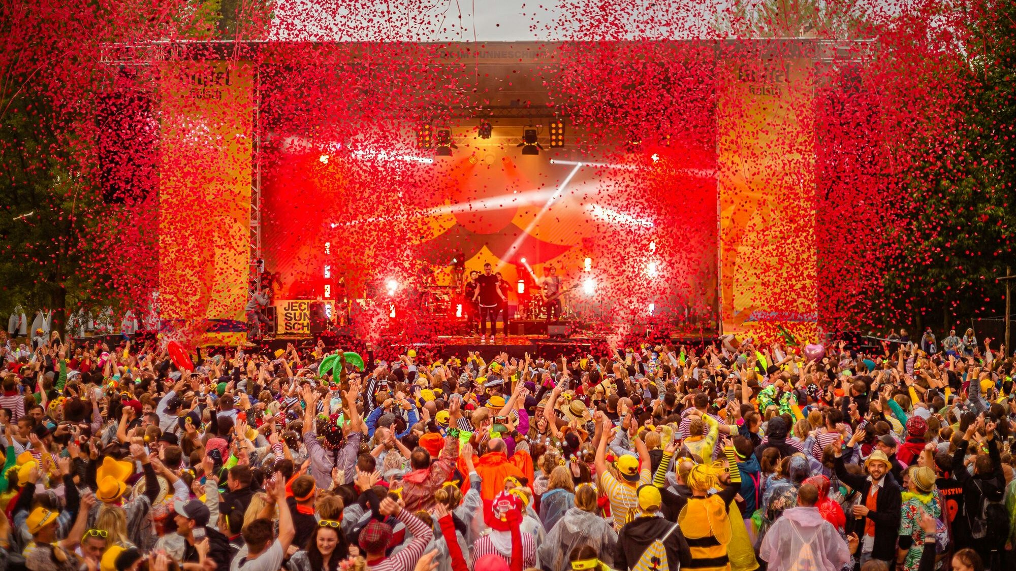 Eine bunt gekleidete Menschenmasse jubelt vor einer Bühne.