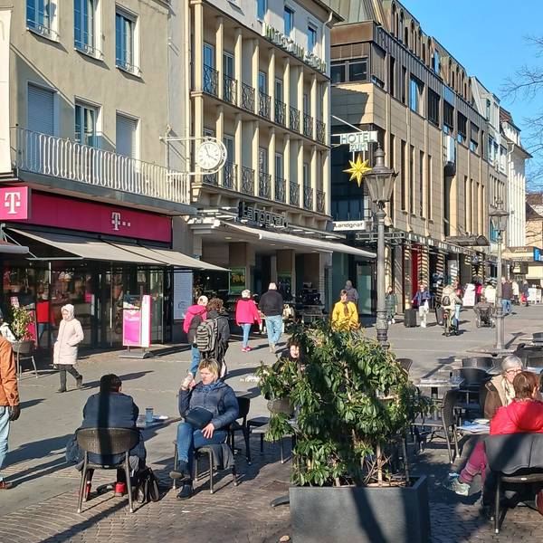 Eine Fußgängerzone im Sonnenlicht, Menschen sitzen im Straßencafé.