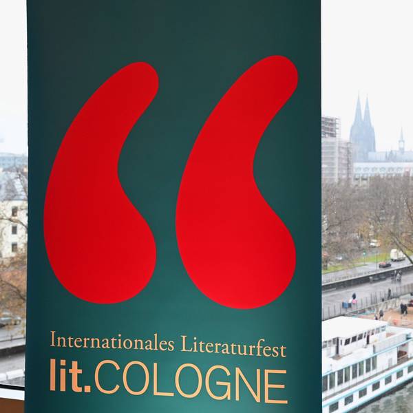 Ein Schild mit dem Logo der lit. Cologne am Rheinufer mit Blick auf den Dom.