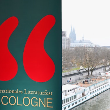 Ein Schild mit dem Logo der lit. Cologne am Rheinufer mit Blick auf den Dom.