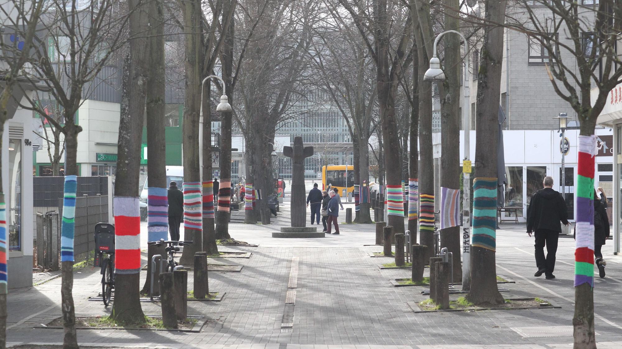 Blick auf die Fußgängerzone. Die Bäume rechts und links haben bunte Strickpullover übergezogen.