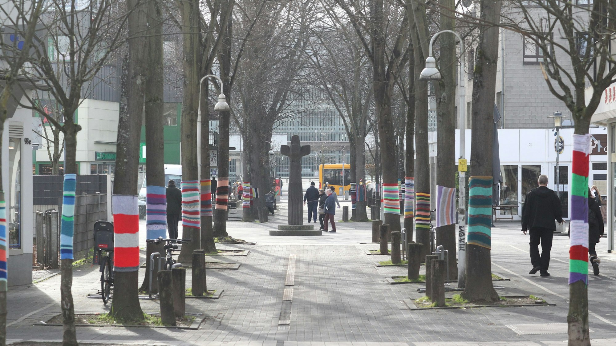 Blick auf die Fußgängerzone. Die Bäume rechts und links haben bunte Strickpullover übergezogen.
