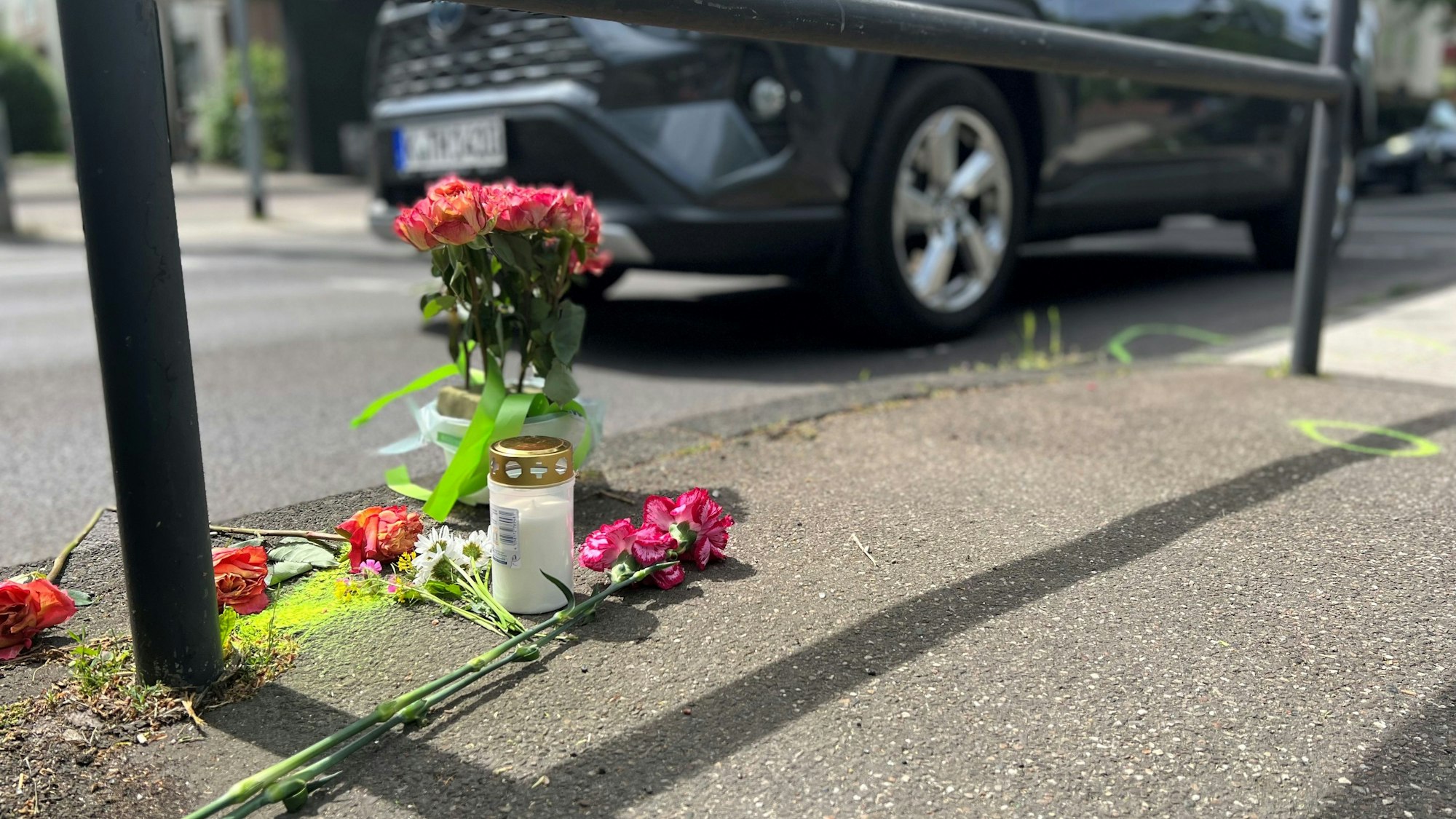 Eine Grabkerze und Rosen stehen am Freitag, 13.05.2022, am Unfallort auf der Aachener Straße in Höhe der Haltestelle Melaten, wo tags zuvor eine 43-jährige Fußgängerin überfahren wurde.