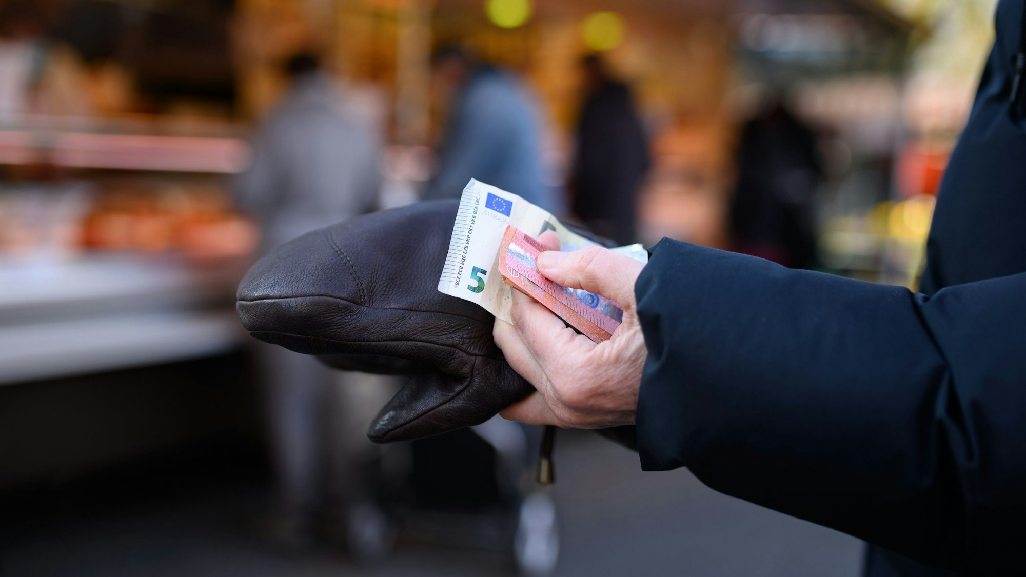 Eine Frau steht an einem Stand an und hält das Bargeld für ihren Einkauf in der Hand bereit.