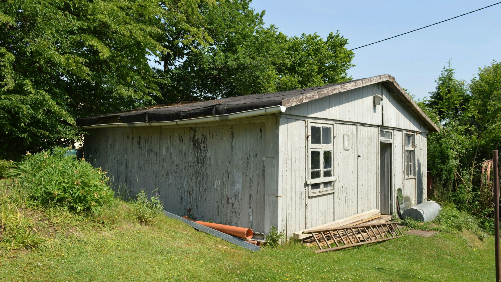 Blick auf eine Baracke aus Holz, die grau angestrichen ist.