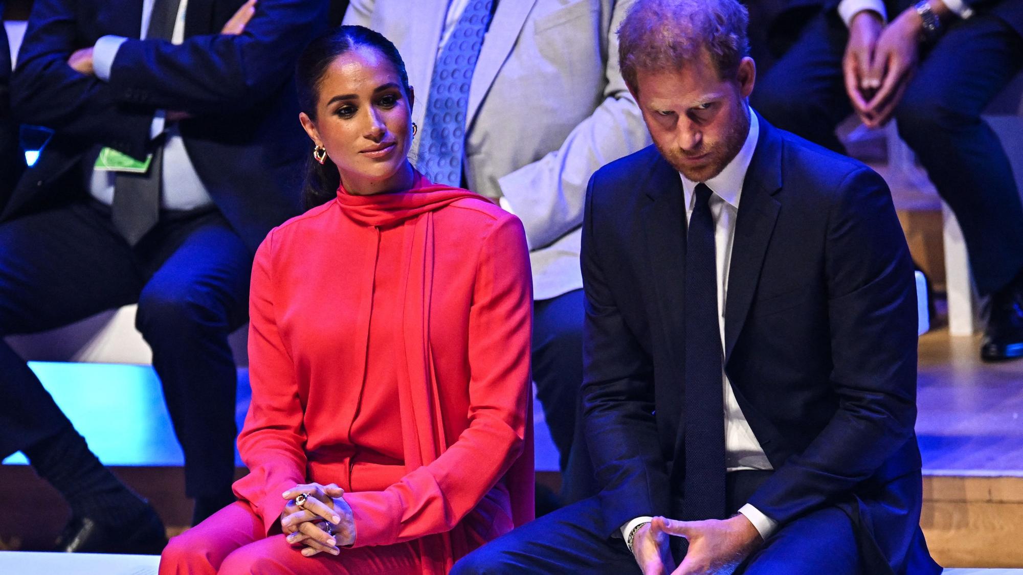 Herzogin Meghan und Prinz Harry sitzen und schauen ernst.