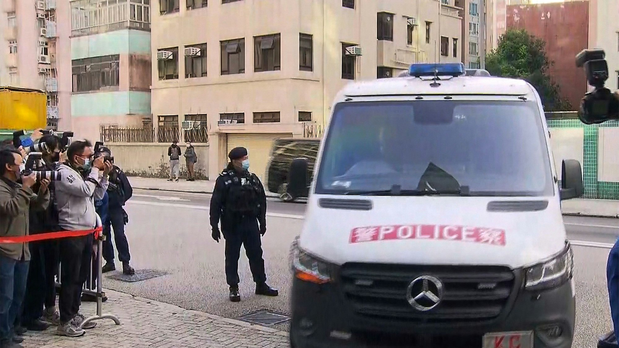 Polizei von Hongkong in einem Wagen, daneben Paparazzis.