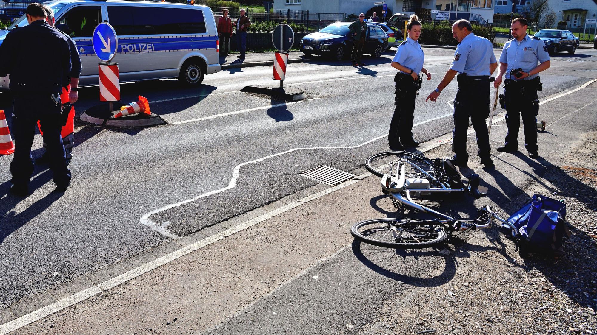 Polizisten stehen auf einer Straße, ein Rad liegt auf dem Boden.