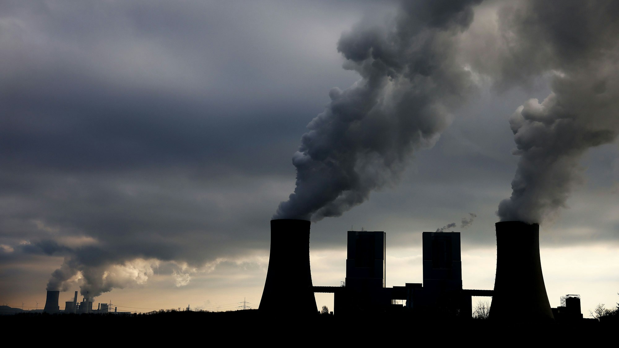 Dampf und Rauch steigt im Gegenlicht aus den Braunkohlekraftwerken Neurath II bei Grevenbroich und Niederaußem auf.