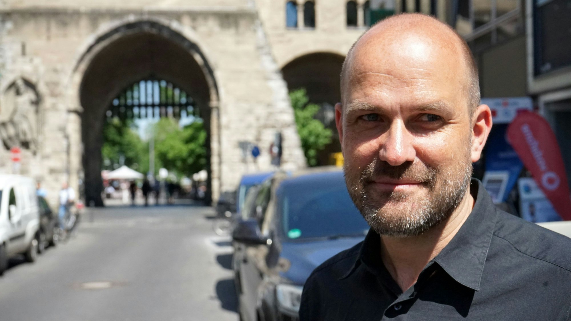 Jan Benden steht vor der Kölner Eigelstein-Torburg und trägt ein schwarzes Hemd.