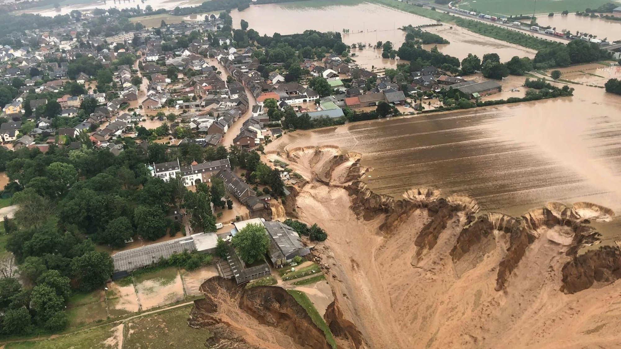 Das Luftbild zeigt die einstürzende Kiesgrube in Blessem, im Hintergrund überschwemmte Flächen.