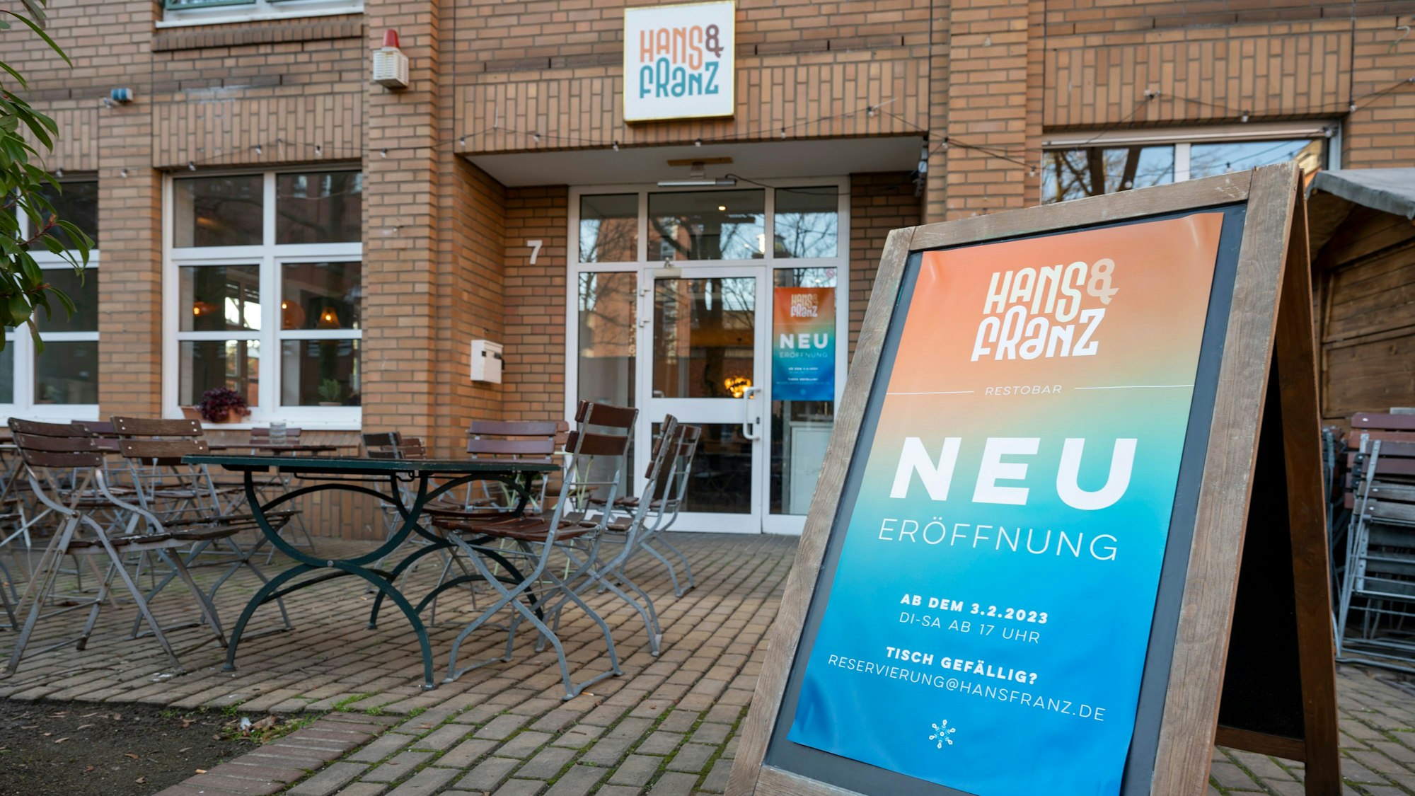 Das „Hans und Franz“ von außen. Auf einem Aufsteller steht Neueröffnung, im Hintergrund sind Tische und Stühle zu sehen.