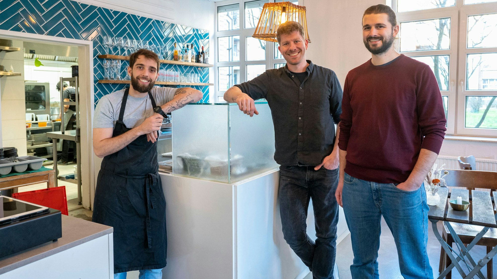Küchenchef Walter Eckerdt und die Inhaber Helge Holzenburg und Florens Holsten stehen in der Restobar am Tresen.