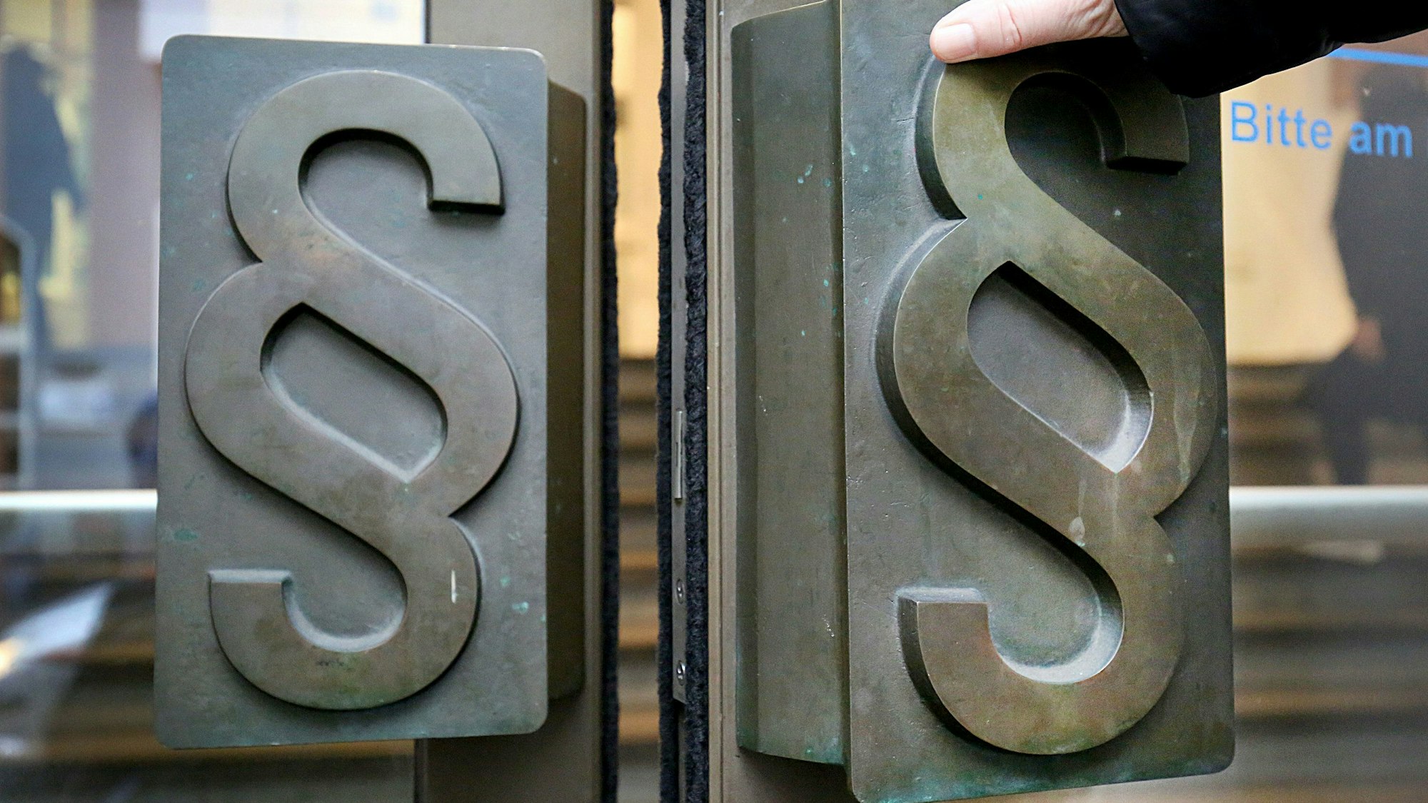 Man sieht die Hand einer Person, die die Türe zum Landgericht auszieht.