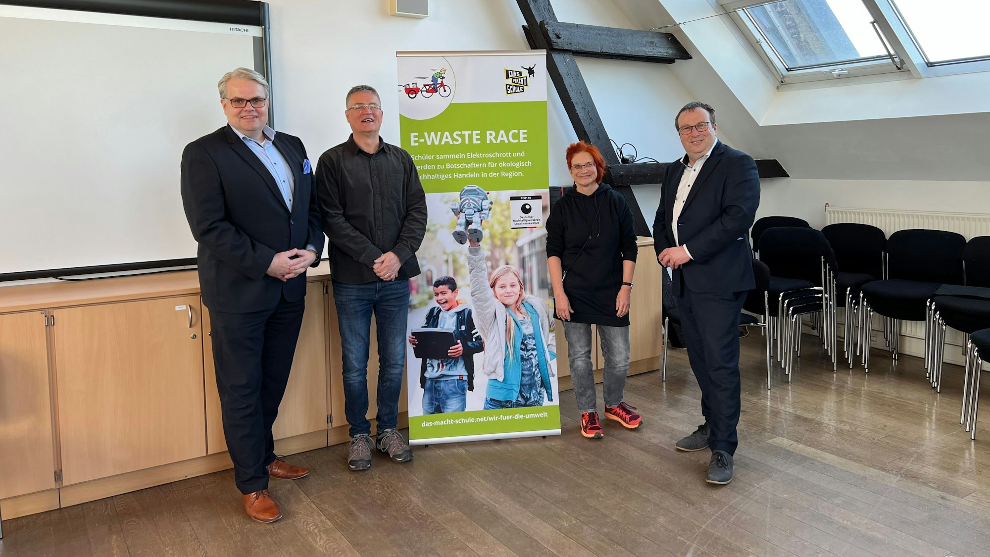 Drei Männer und eine Frau stehen vor einem Banner.