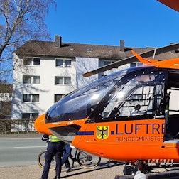 Ein Kind in Matschhose und mit Mütze sitzt mit baumelnden Beinen in der offenen Tür eines Helikopters der Luftrettung.