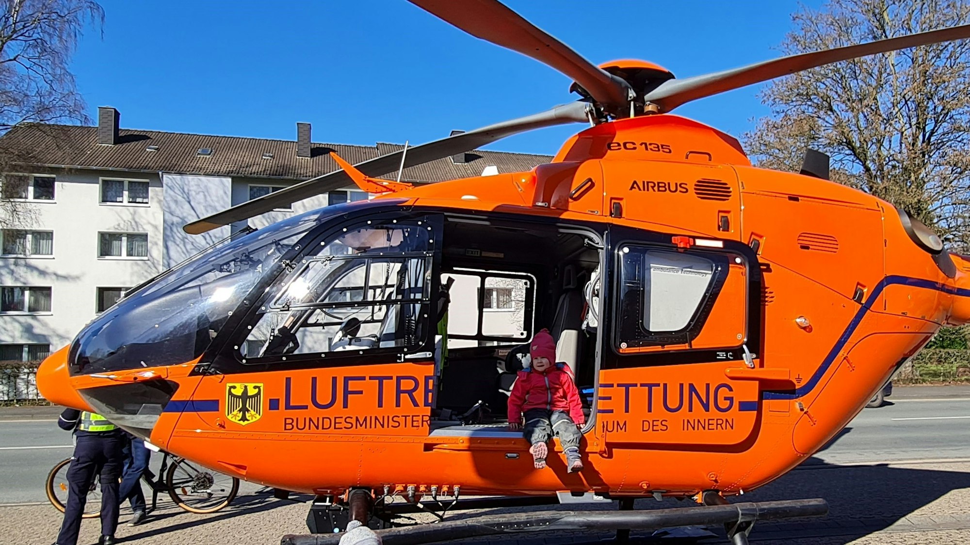 Ein Kind in Matschhose und mit Mütze sitzt mit baumelnden Beinen in der offenen Tür eines Helikopters der Luftrettung.