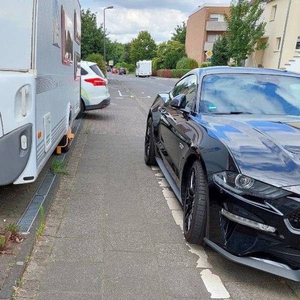 Zugeparkter Gehweg mit extrem schmalem Pfad zwischen Pkw und Wohnwagen.