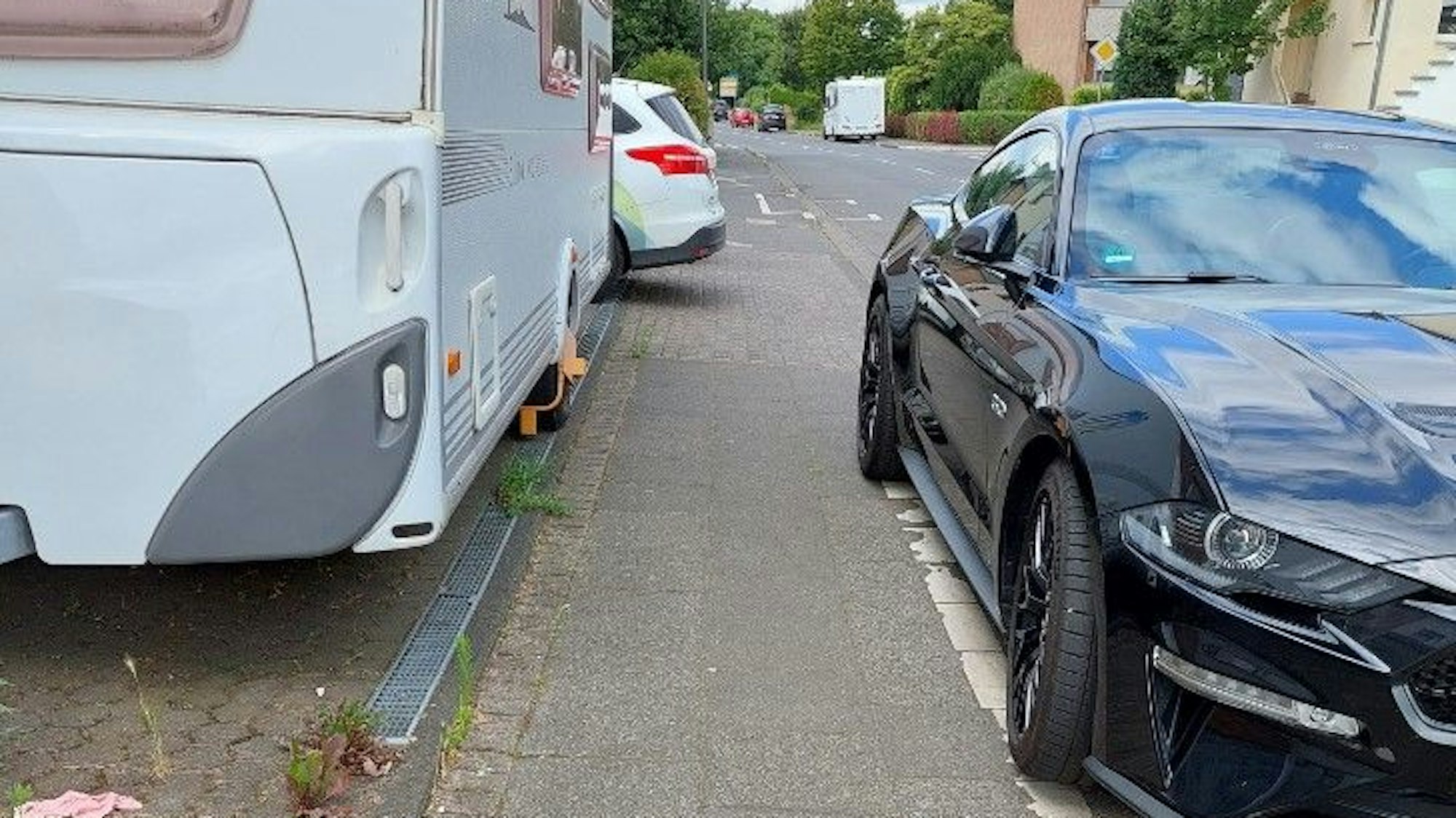 Zugeparkter Gehweg mit extrem schmalem Pfad zwischen Pkw und Wohnwagen.