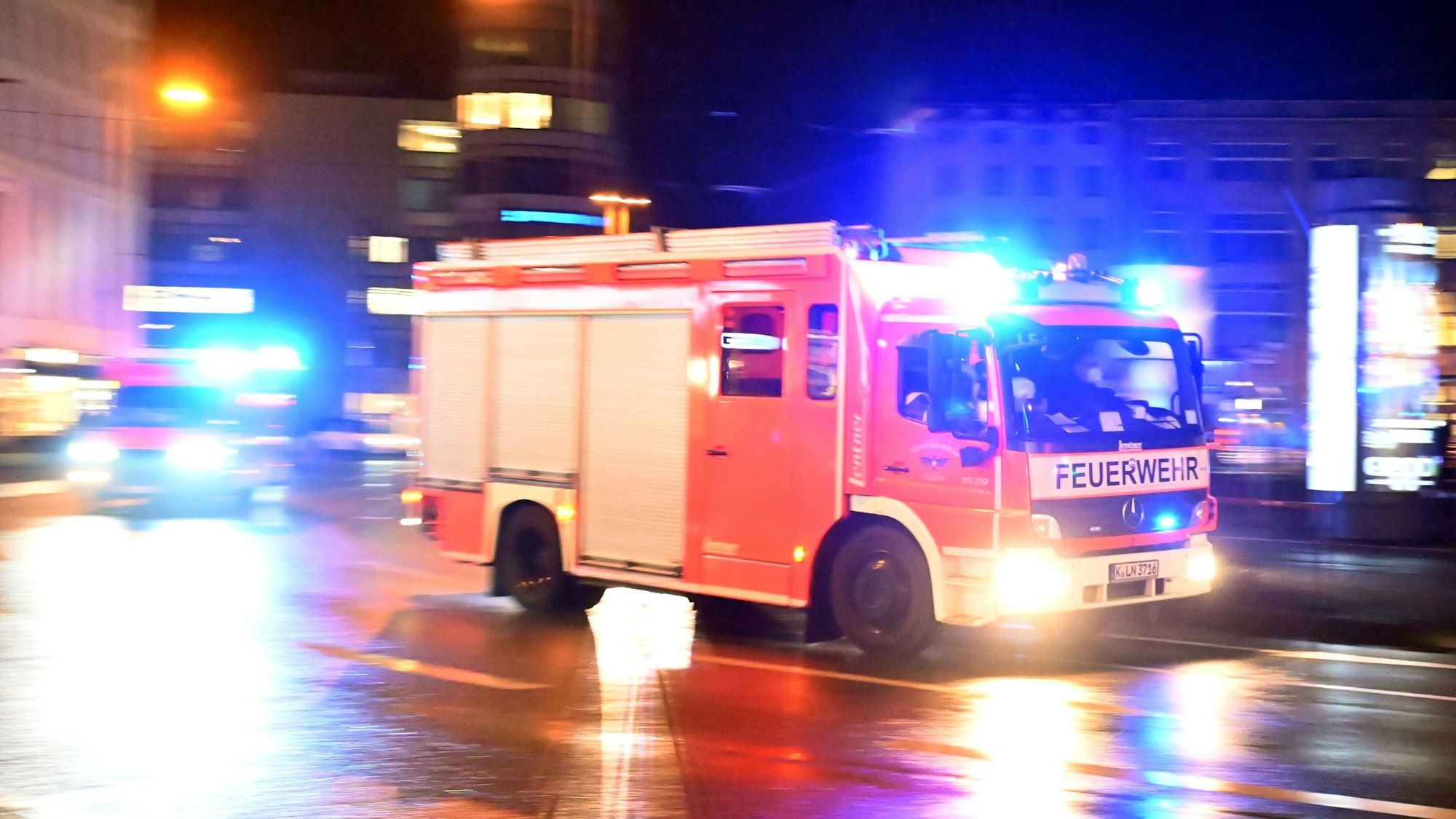 Ein Feuerwehrwagen rast im Dunkeln über eine nasse Straße.