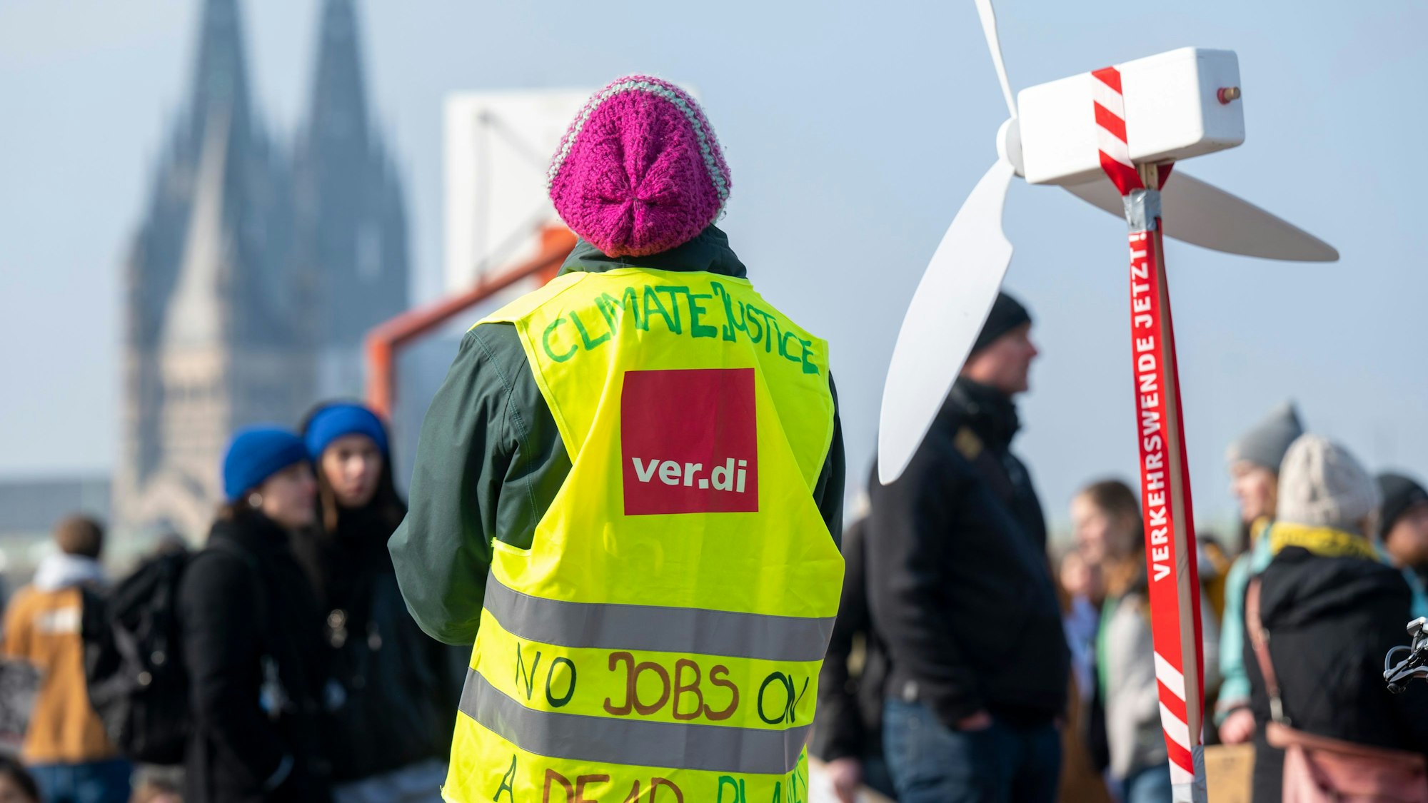 Ein Mensch in Verdi-Warnweste steht neben einem selbstgestalteten Windrad. Im Hintergrund ist der Dom zu sehen.