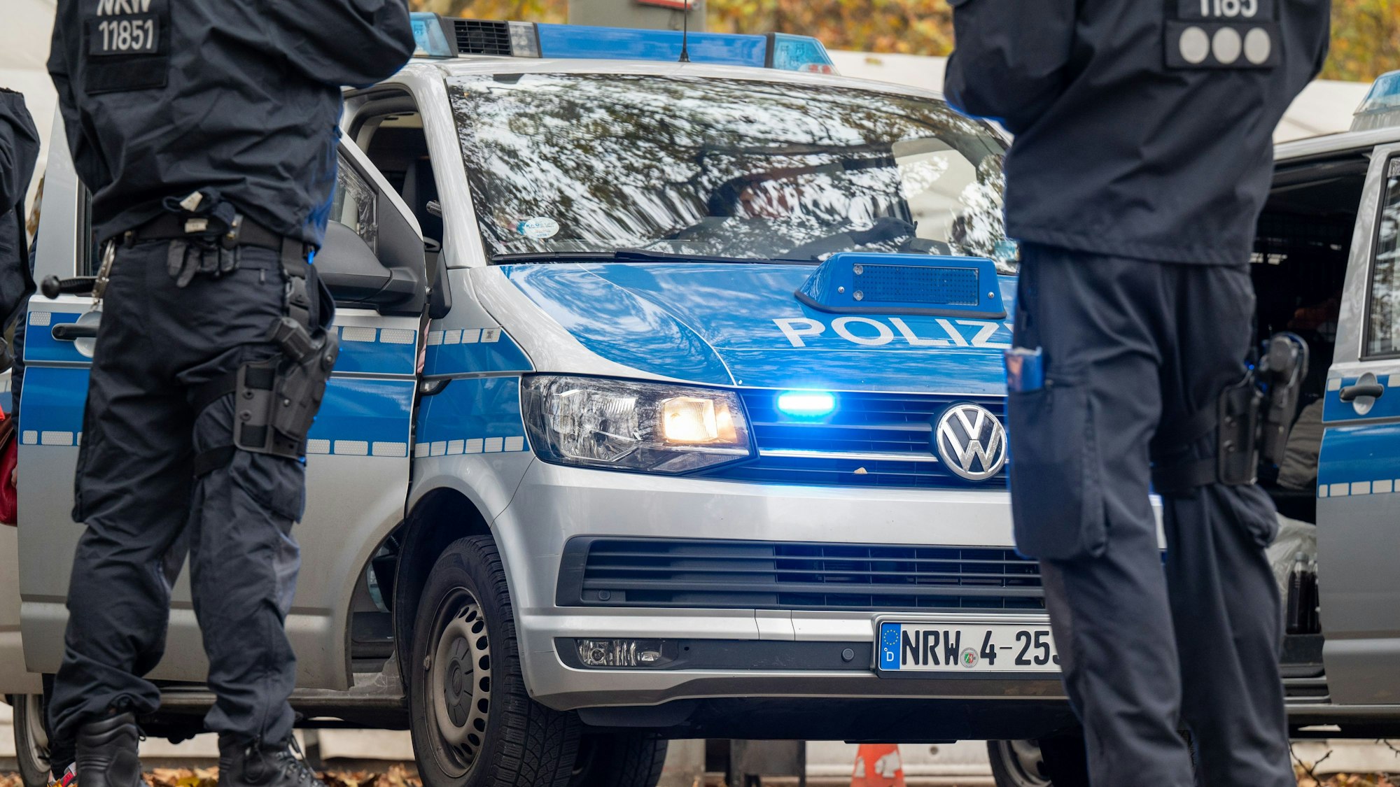 Polizisten stehen vor einem Einsatzfahrzeug der Polizei.