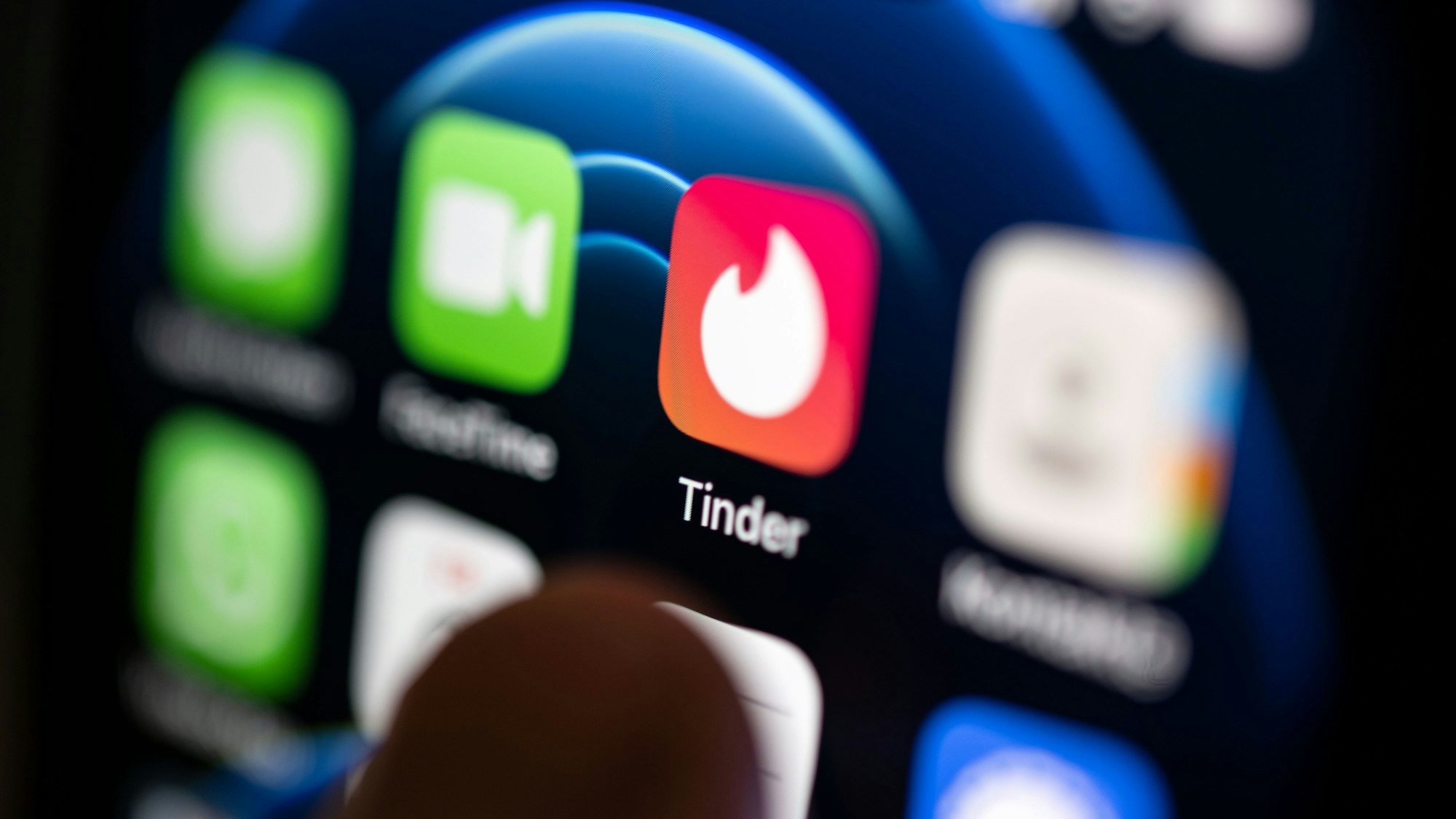 Ein Finger bedient ein Smartphone, auf dem unter anderen die App von Tinder installiert ist.