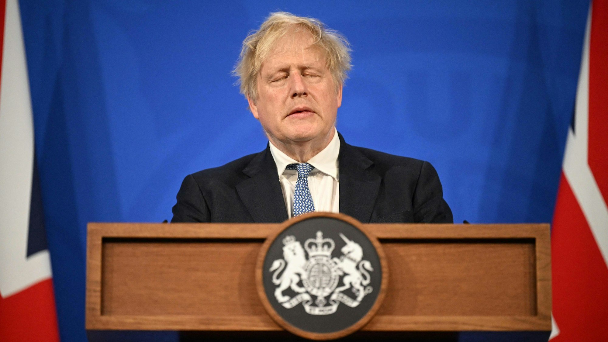 Boris Johnson mit geschlossenen Augen bei einer Pressekonferenz.