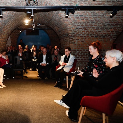 Die Teilnehmerinnen und Teilnehmer sitzen in einem gemauerten Kellergewölbe auf Sesseln.
