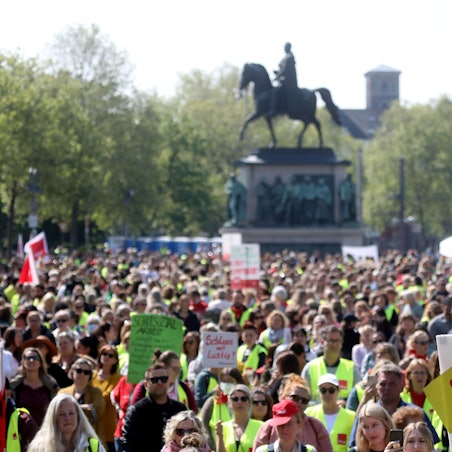 Kommunale Sozialarbeiterinnen und Sozialarbeiter sowie Erzieherinnen und Erzieher sind mit Warnwesten und Plakaten auf dem Kölner Heumarkt bei einer Kundgebung versammelt.