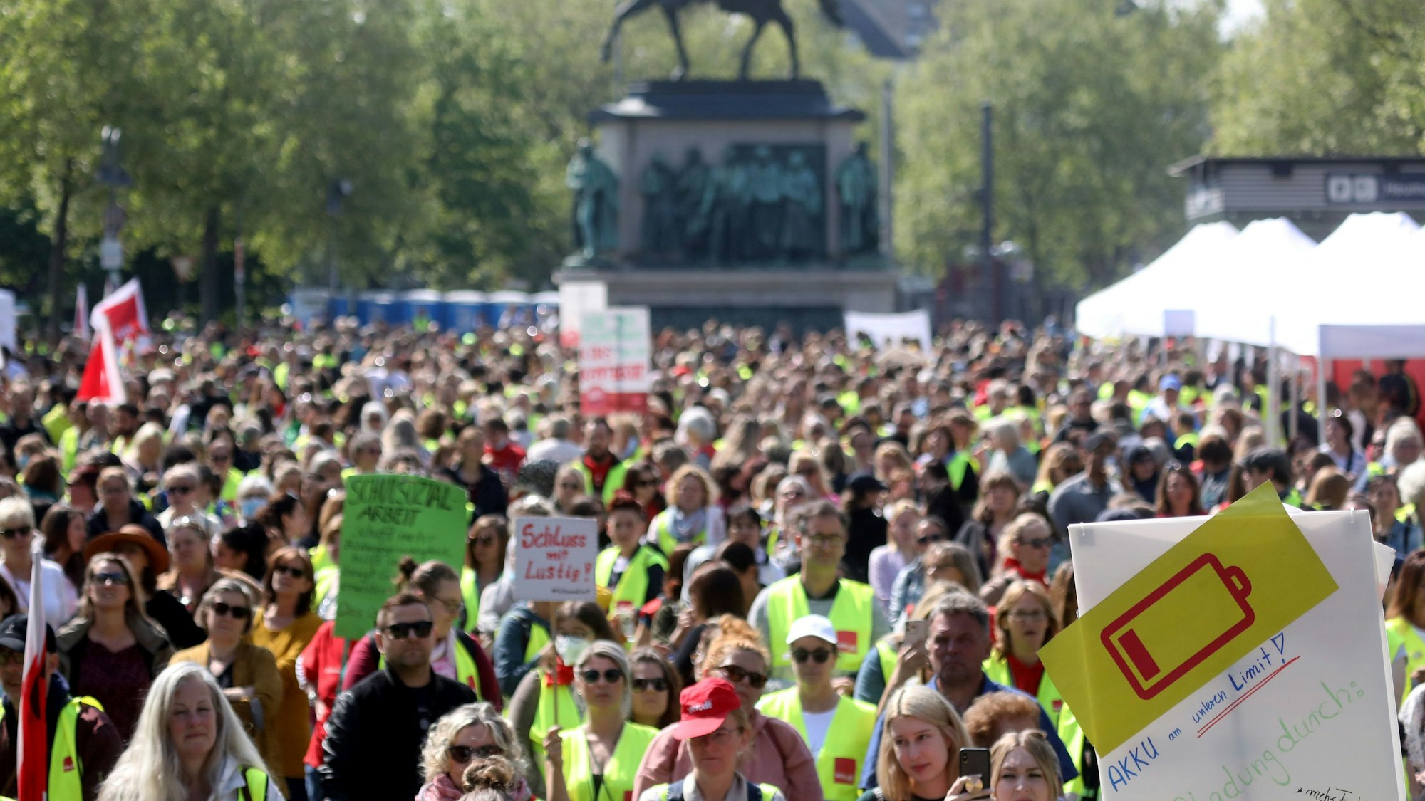 Kommunale Sozialarbeiterinnen und Sozialarbeiter sowie Erzieherinnen und Erzieher sind mit Warnwesten und Plakaten auf dem Kölner Heumarkt bei einer Kundgebung versammelt.