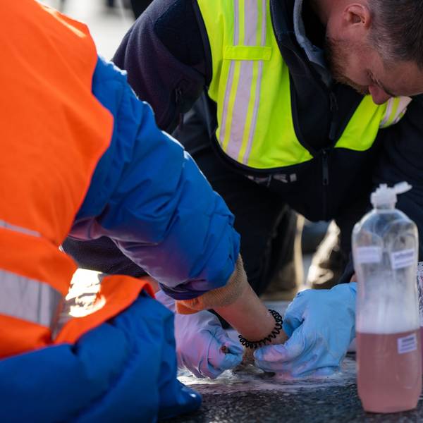 Ein Polizist löst die festgeklebte Hand eines Klimaaktivisten, der sich zuvor auf eine Straße geklebt hat.