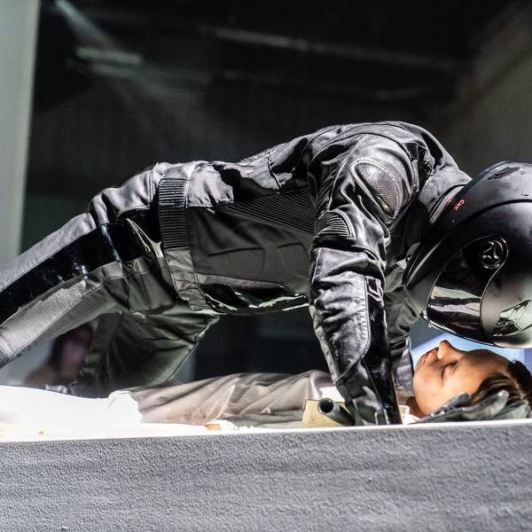 Der Schauspieler Justus Maier beugt sich im schwarzen Motrorrad-Anzug mit Helm über eine Statistin. Szene aus Robert Borgmanns „Meta-Sleep“, eine musiktheatrale Installation nach Motiven von »Leonce und Lena« am Schauspiel Köln.