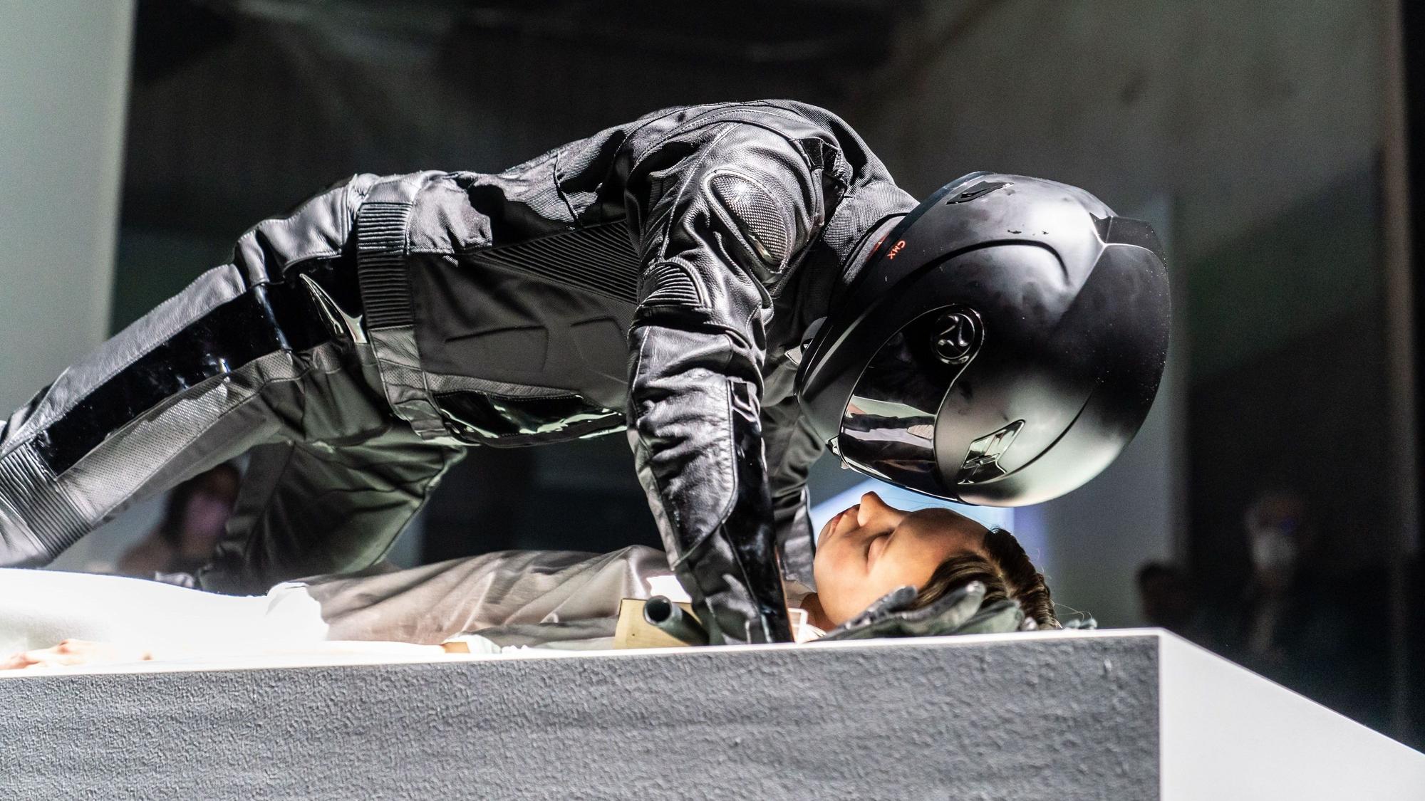 Der Schauspieler Justus Maier beugt sich im schwarzen Motrorrad-Anzug mit Helm über eine Statistin. Szene aus Robert Borgmanns „Meta-Sleep“, eine musiktheatrale Installation nach Motiven von »Leonce und Lena« am Schauspiel Köln.