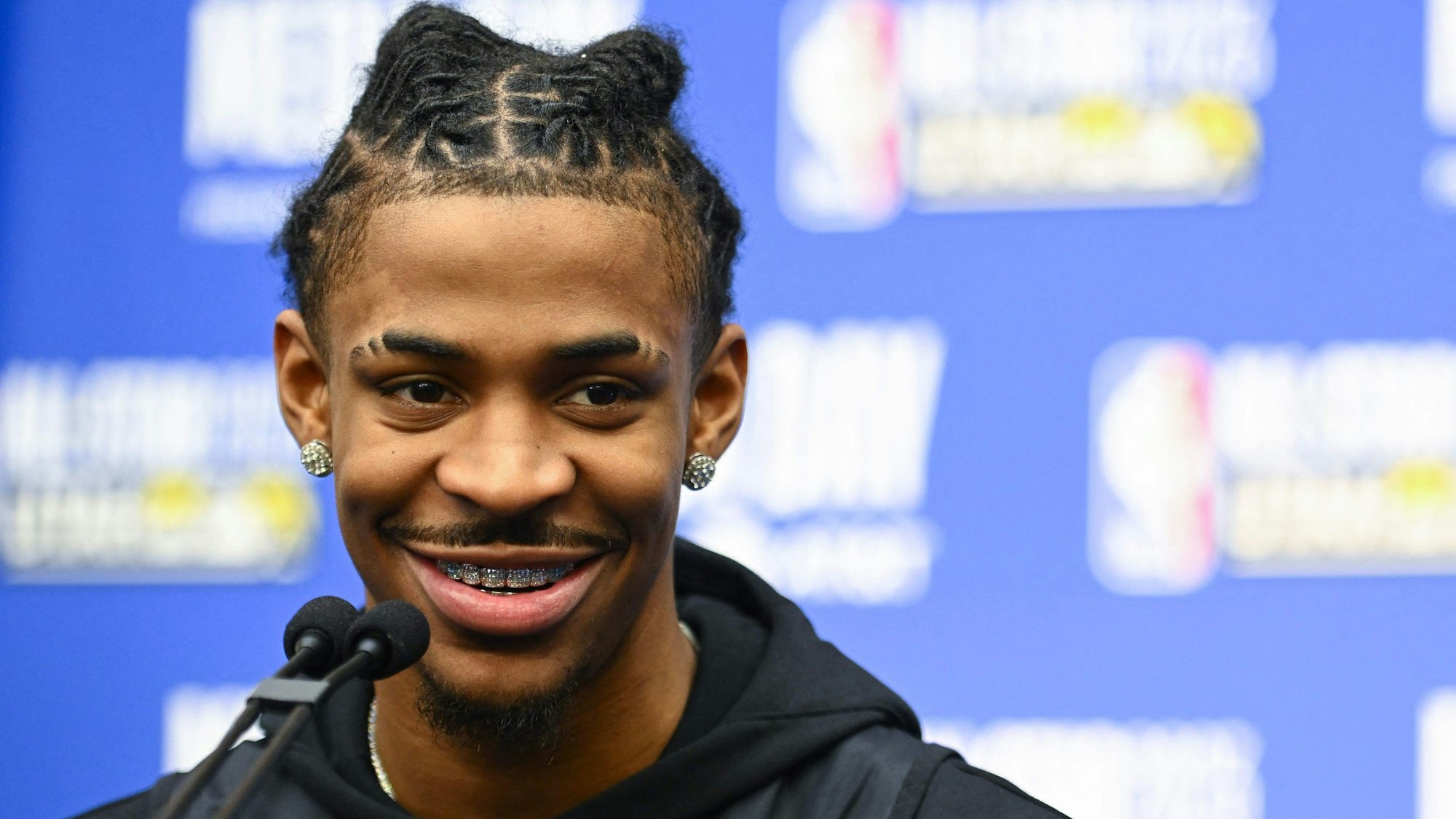 Ja Morant beantwortet Fragen auf einer Pressekonferenz. Er lächelt, vor ihm ist ein Mikrofon.