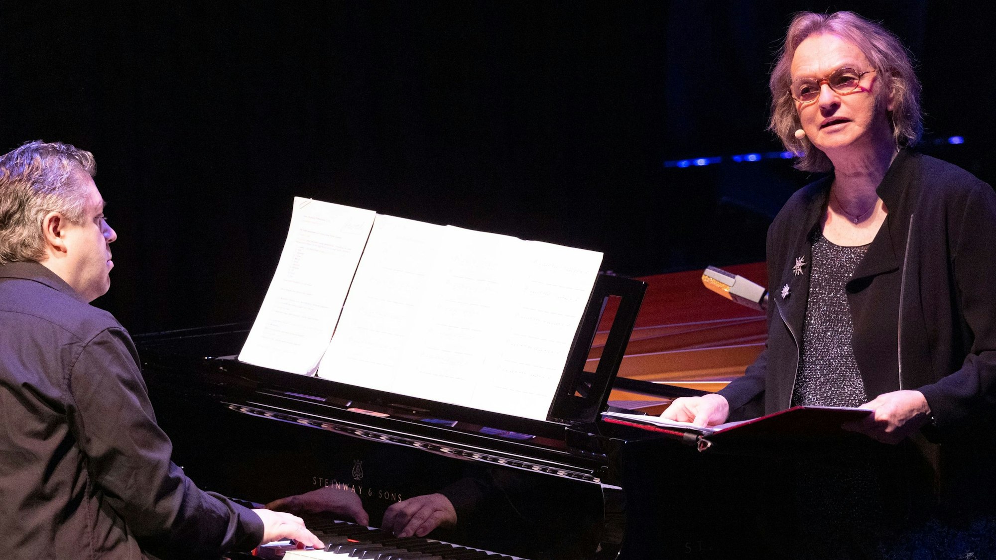 Der Musiker Marc-Aurel Floros sitzt am Flügel und Elke Heidenreich steht mit einer Mappe in der Hand daneben.