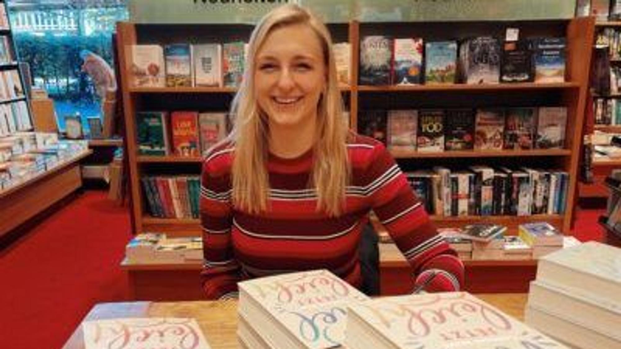 Die Autorin Carolin Wahl sitzt in einer Buchhandlung und lächelt in die Kamera. Vor ihr liegen Ausgaben ihres Buchs „Vielleicht jetzt“.
