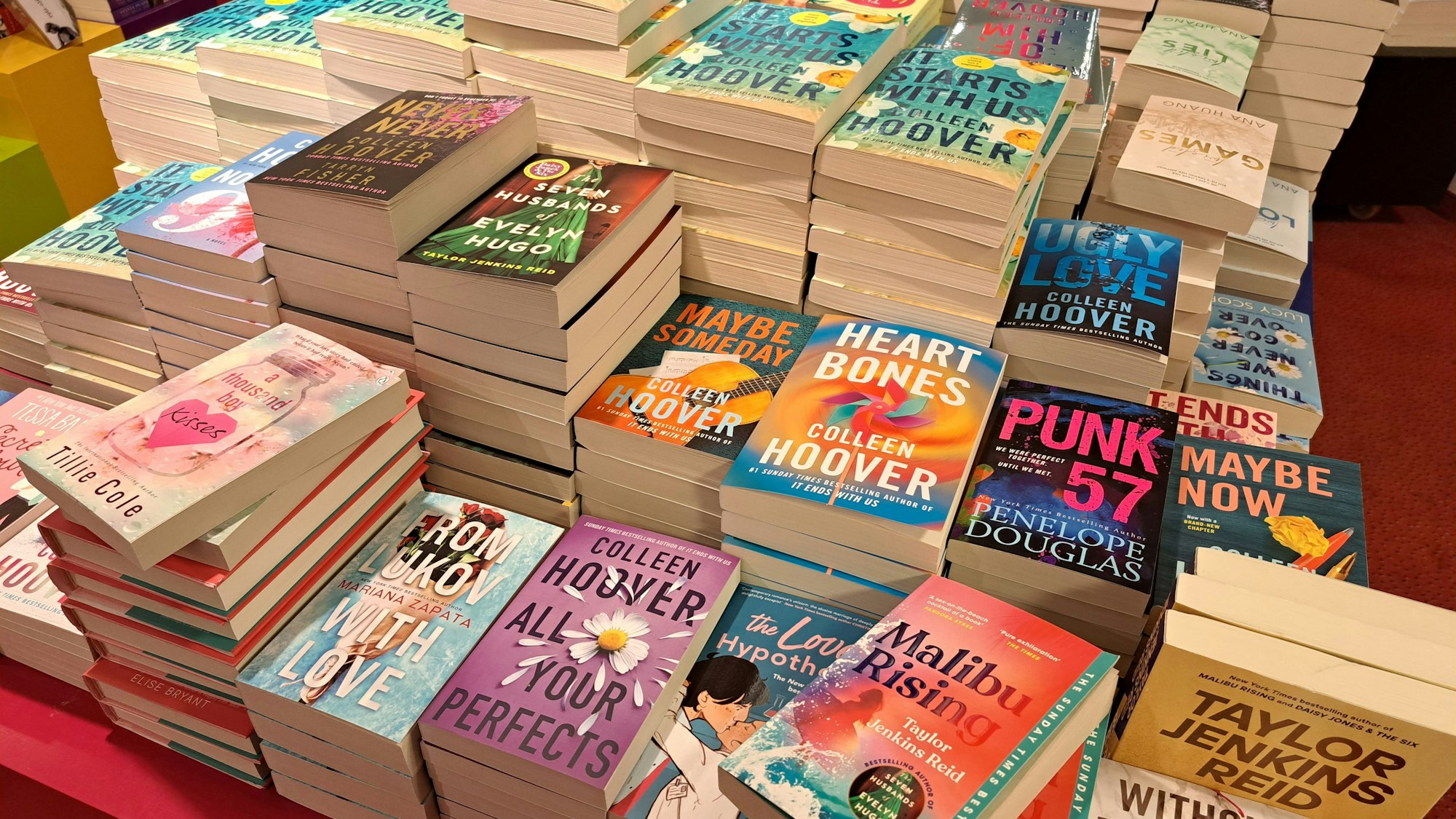 Sicht auf einen Thementisch in der Mayersche-Buchhandlung am Neumarkt. Romance und New-Adult-Bücher, die von TikTok bekannt sind, stapeln sich. Mit dabei sind etliche Bücher von Colleen Hoover, die Spitzenreiterin der BookTok-Autorinnen ist, Taylor Jenkins Reid, Ali Hazelwood und Penelope Douglas.