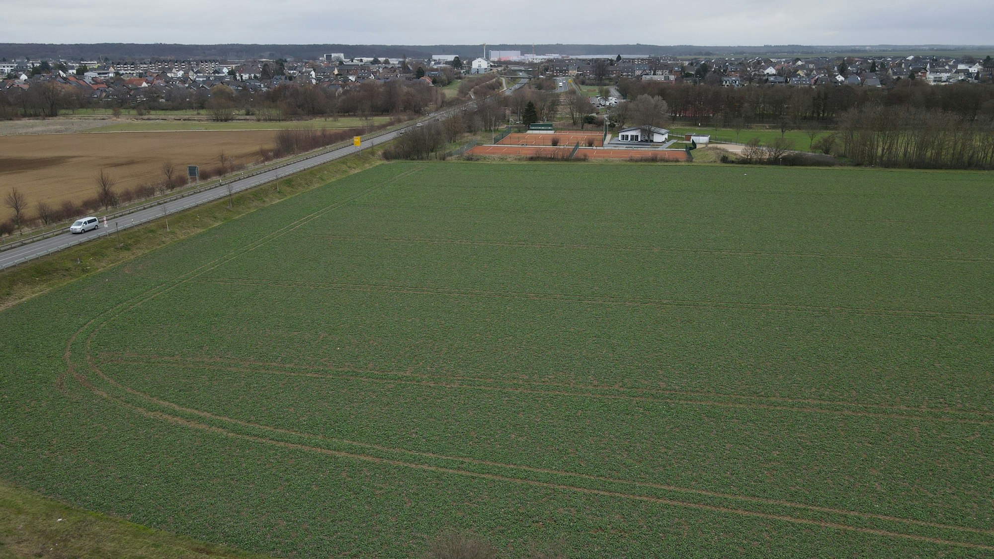 Eine Aufnahme von schräg oben zeigt ein unbebautes Feld an einer Straße, über die ein Auto fährt.