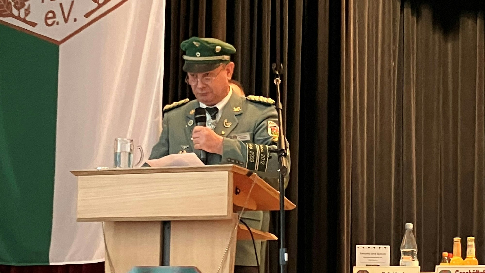 Ein Mann in grüner Schützenuniform steht mit Mikrofon in der Hand an einem Rednerpult.