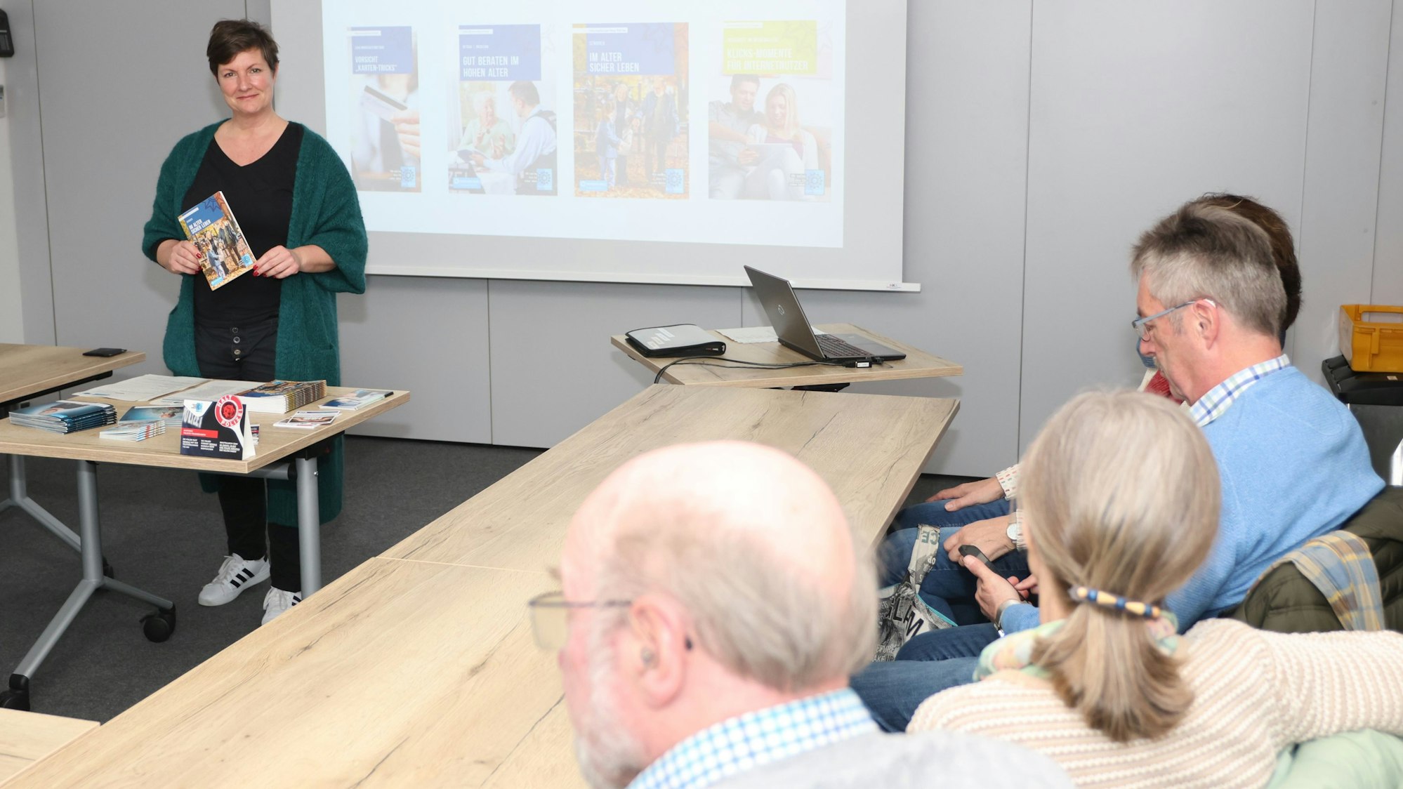 Eine Frau hält einen Vortrag. Einige ältere Besucher hören ihr zu.