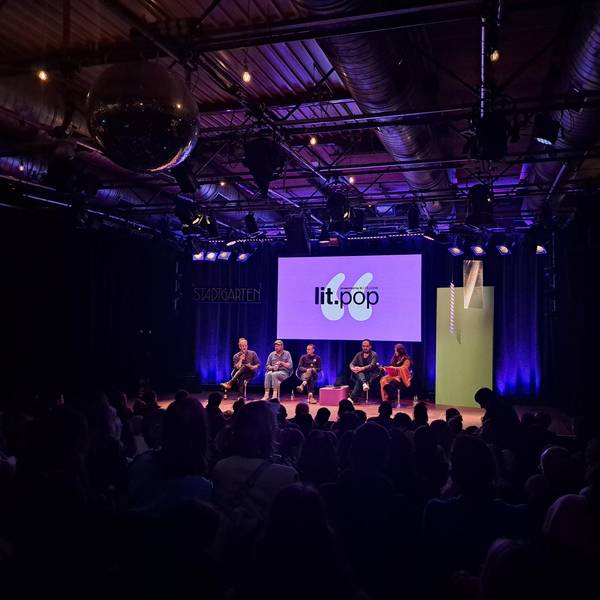 Valentin Moritz (links), Philipp Winkler, Joris Bas Backer, Dinçer Güçyeter und Mithu Sanyal bei der lit.pop im Kölner Stadtgarten am 4. März. Sie sitzen in der Reihe auf der Bühne. Hinter ihnen ist das lilane Logo der lit.pop groß auf einem Bildschirm. Vor ihnen sitzt das Publikum.