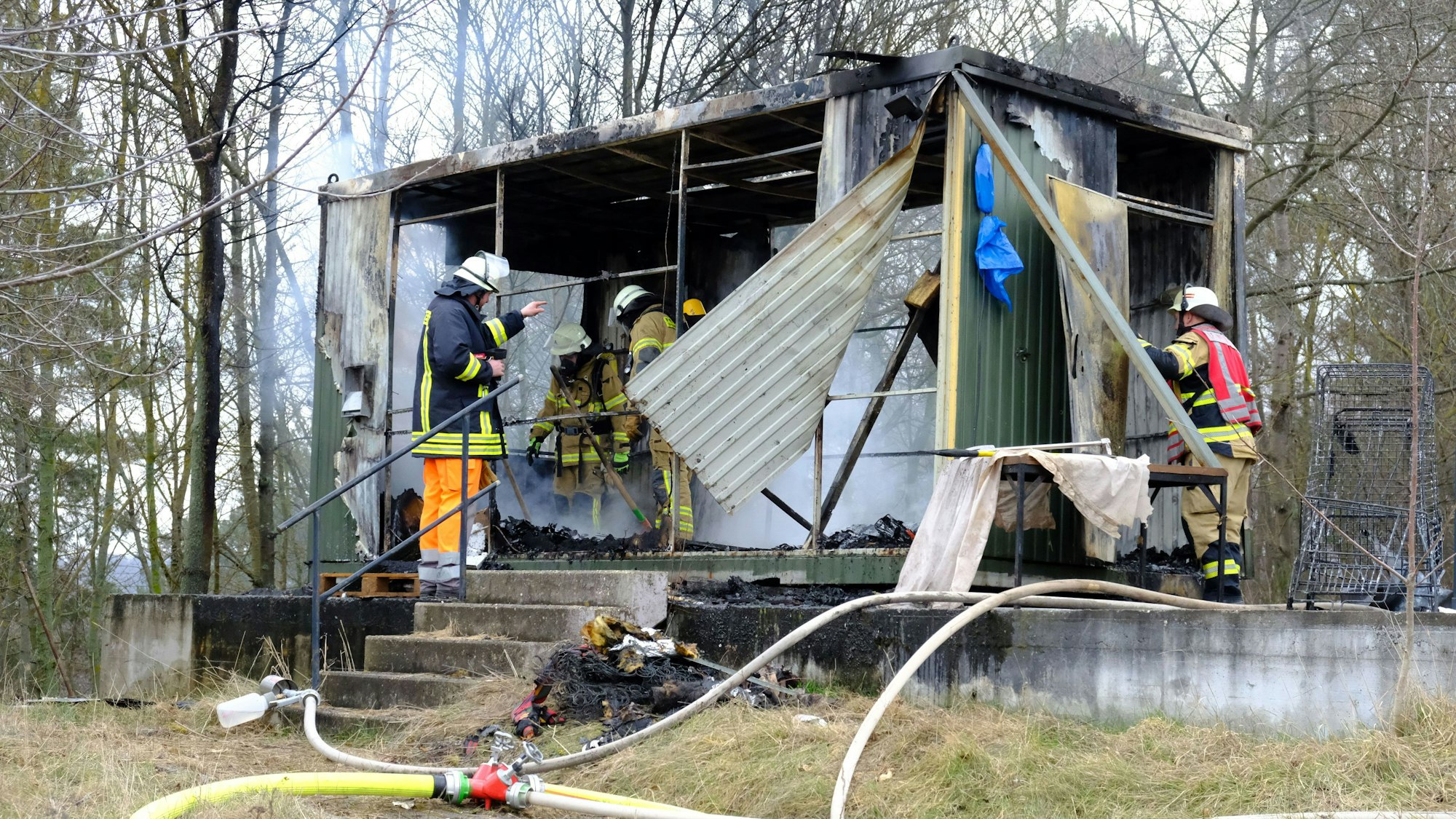 Man sieht Einsatzkräfte, wie sie die letzten Brandherde im Container löschen.