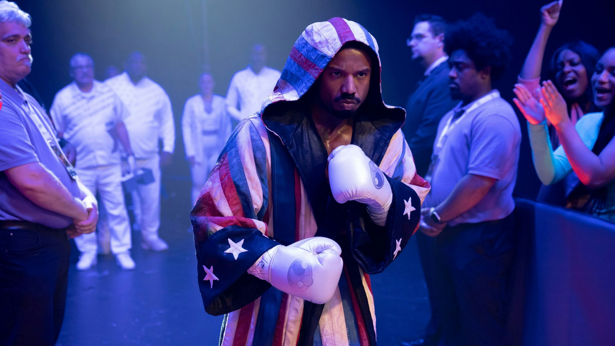 Ein Mann mit Boxhandschuhen und Mantel geht an vielen Menschen vorbei.