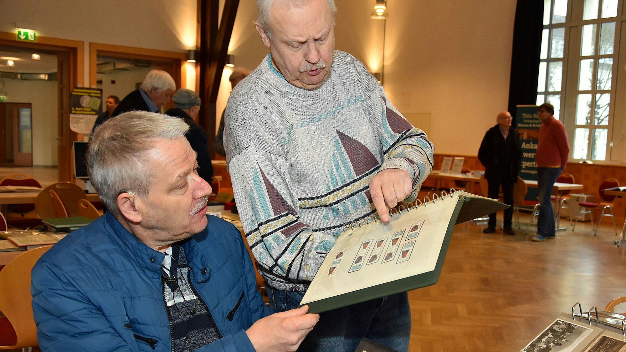 Zwei Sammler betrachten ein Album mit Briefmarken.